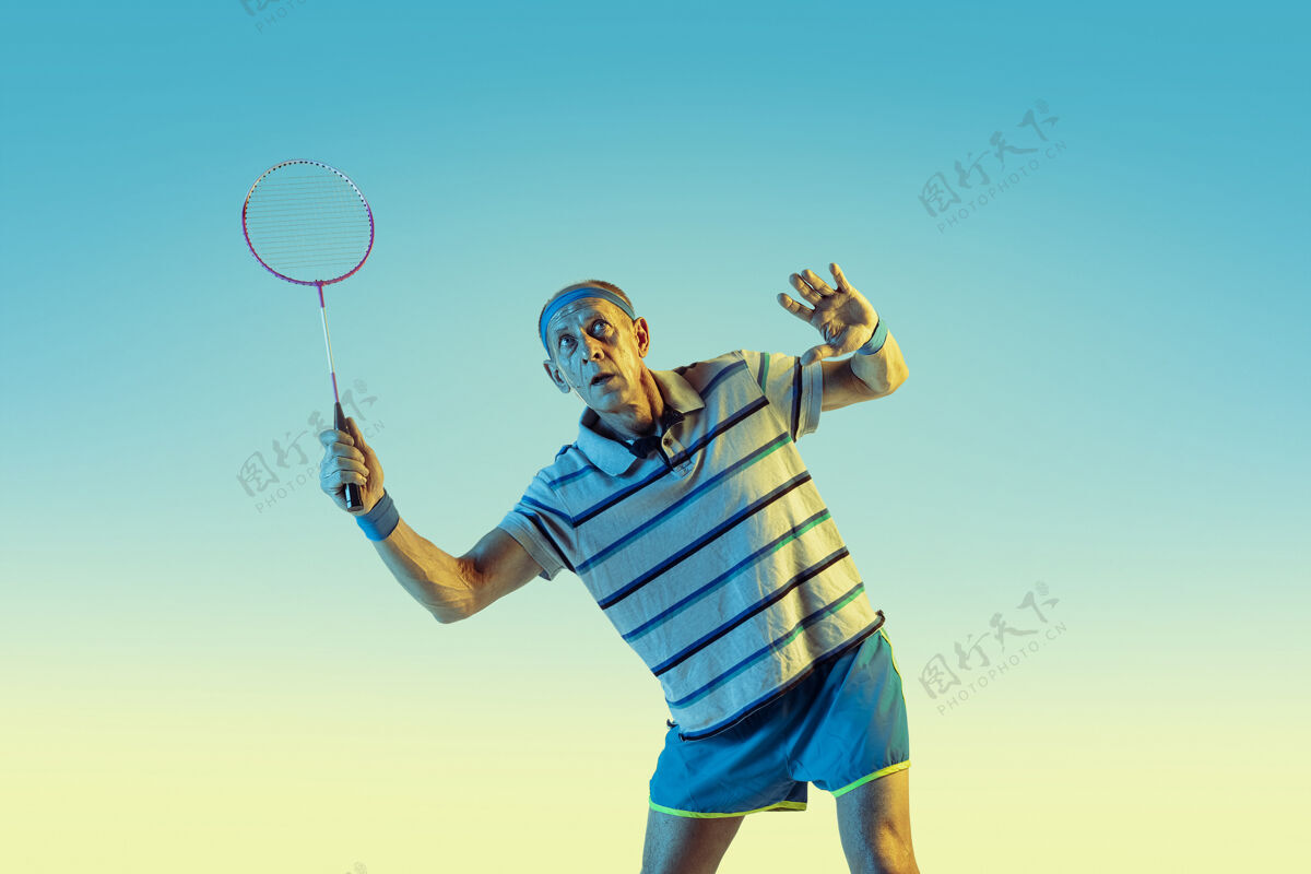 老年人穿运动服的高级男士在梯度背景下打羽毛球 霓虹灯身材魁梧的白人男模保持活跃运动 活动 运动 健康 自信的概念健康球拍运动装