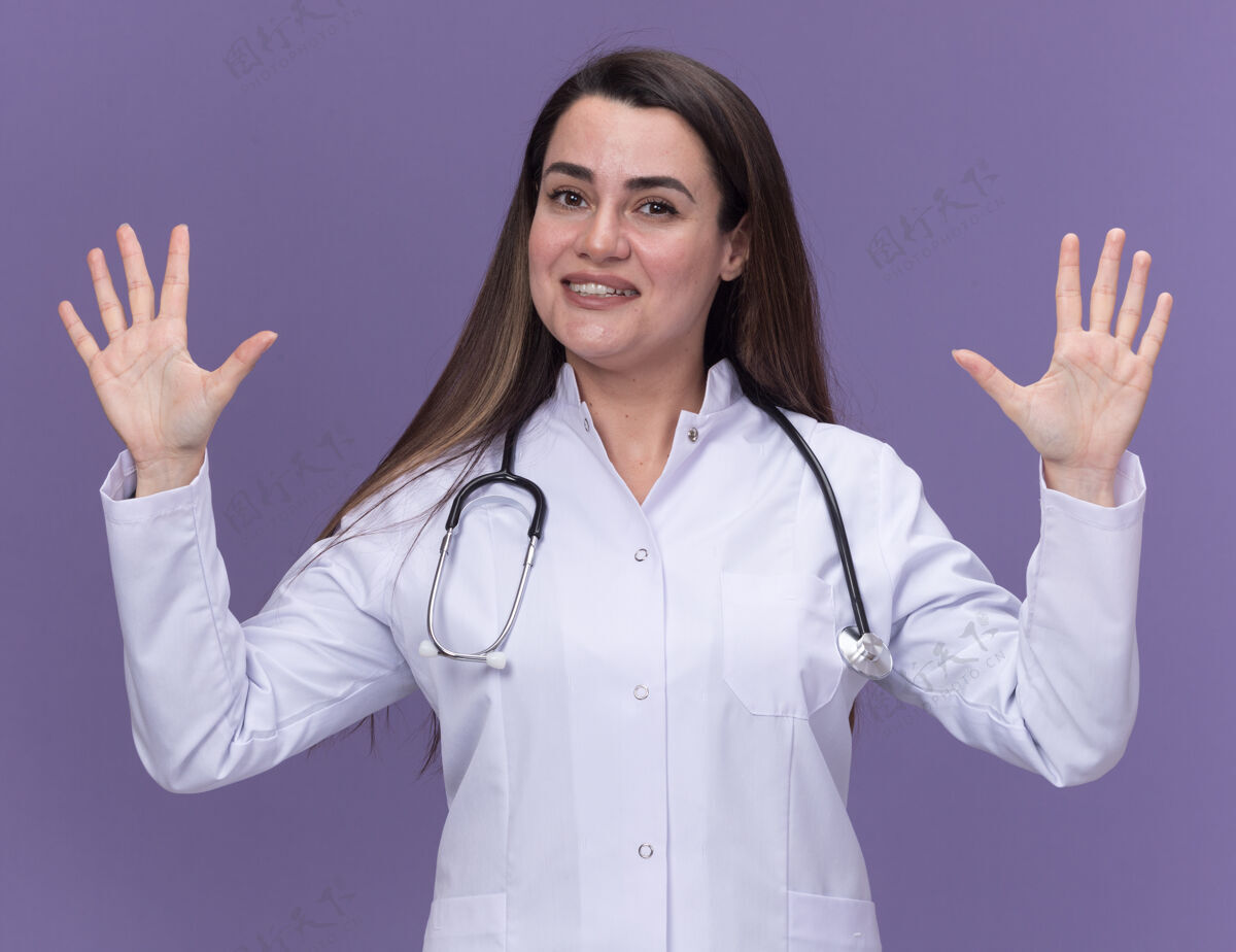 长袍面带微笑的年轻女医生身穿医用长袍 手持听诊器 举手站立紫色微笑穿上