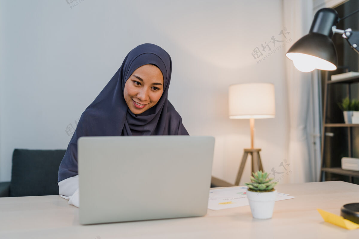 办公桌美丽的亚洲穆斯林女士戴着头巾 穿着休闲服 在夜总会的客厅里使用笔记本电脑房子商务女性穆斯林