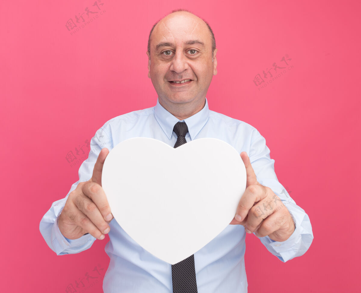 人微笑着的中年男子身穿白色t恤 打着领带 在粉红色的墙上对着镜头伸出心形盒子人人抱着