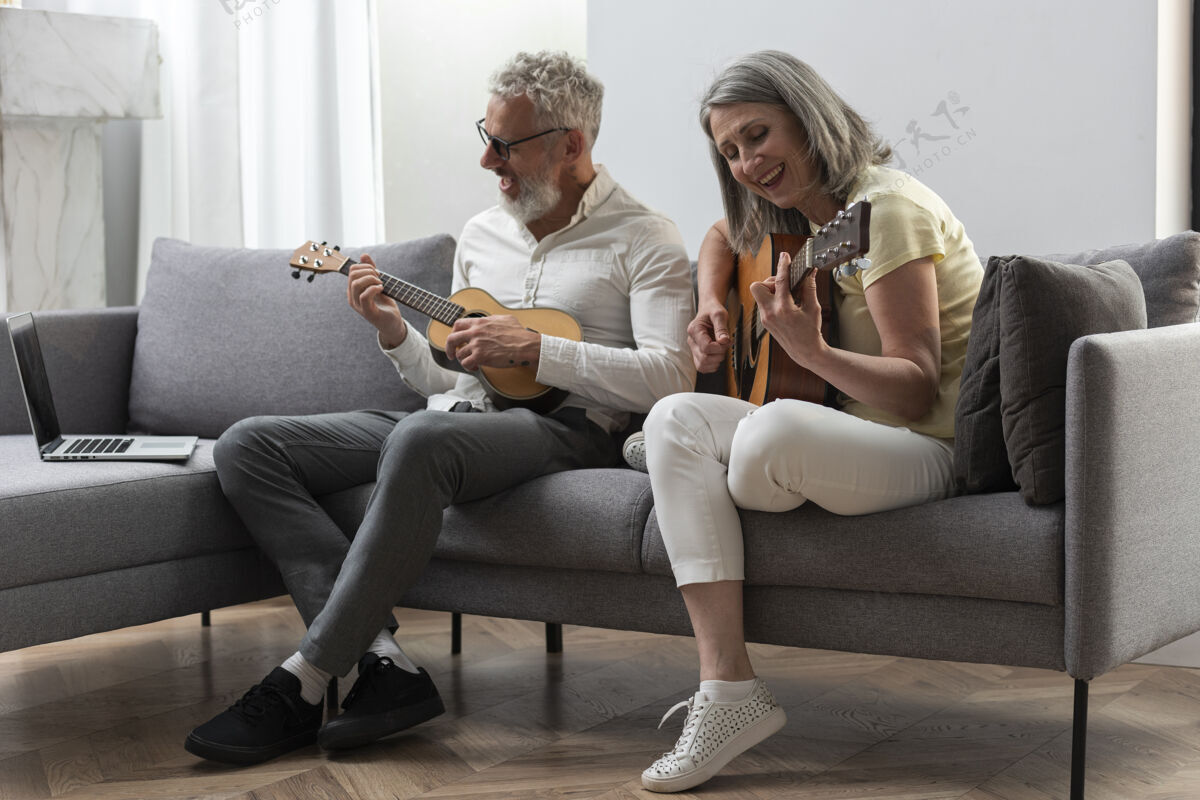 室内资深夫妇在家学习吉他和四弦琴课程的笔记本电脑沙发水平灰色头发
