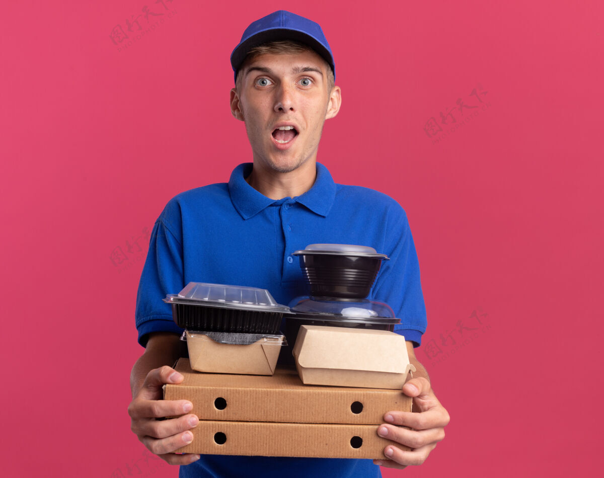 粉红色令人印象深刻的年轻金发送货男孩举行食品容器和包装比萨饼盒披萨盒子食物