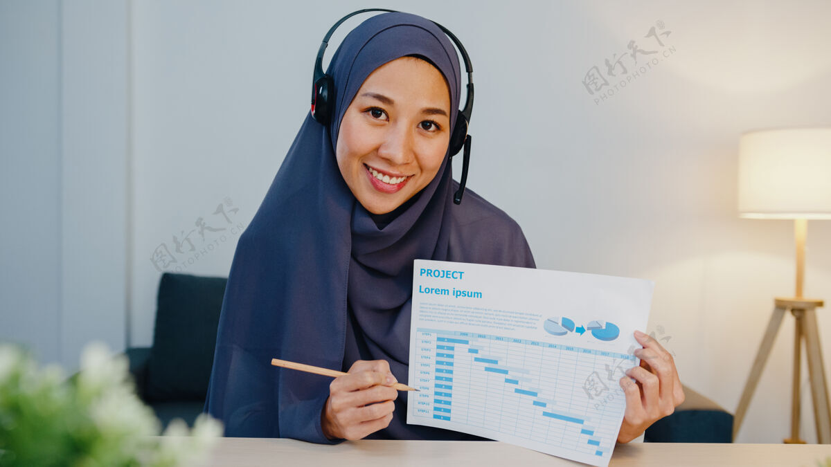 围巾穆斯林女士戴着耳机 用笔记本电脑 晚上在家办公的时候 在电话会议上和同事谈论销售报告在线商务人员