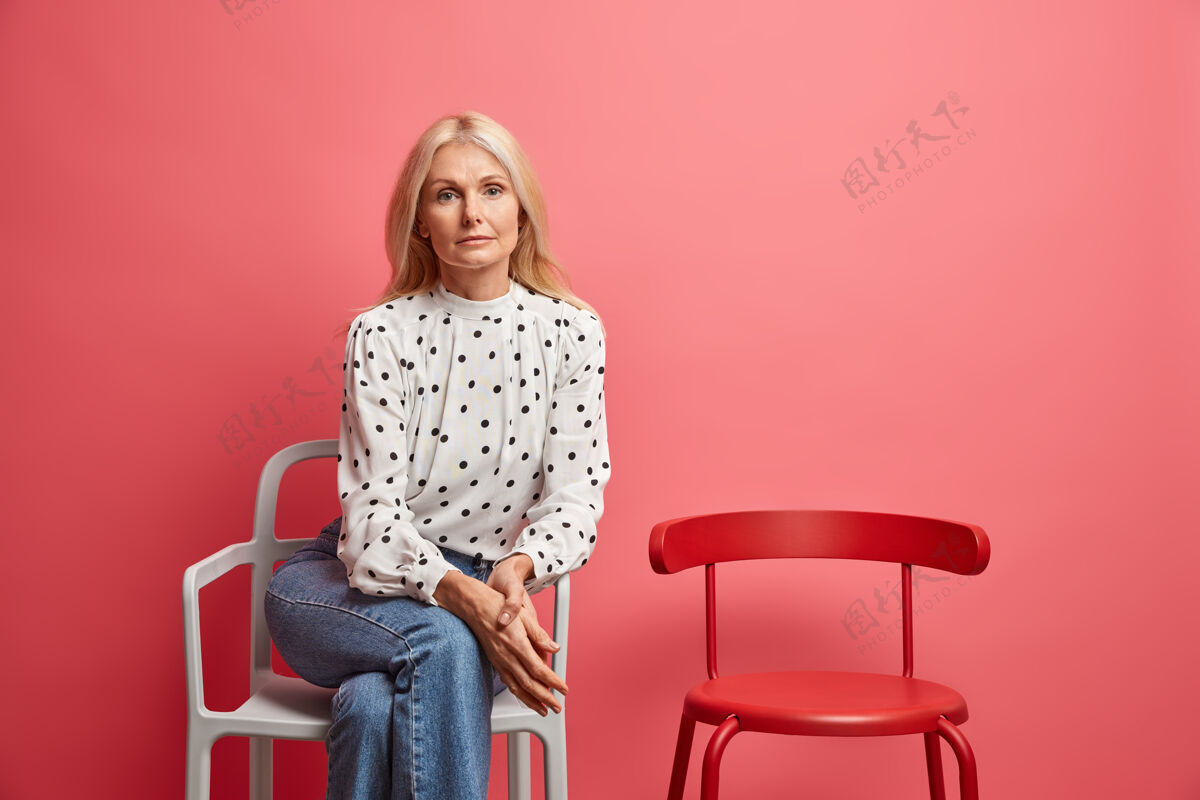 表情女人打扮得漂漂亮亮地坐在舒适的椅子上 独自一人在鲜亮的粉红色上排队等候成人罗西女性