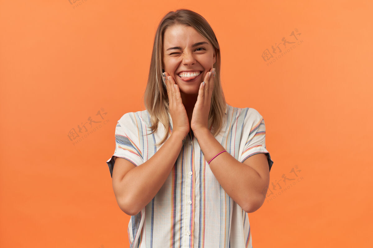 快乐快乐俏皮的年轻女子在条纹衬衫眨眼和显示舌头孤立在橙色的墙壁表情乐趣玩耍