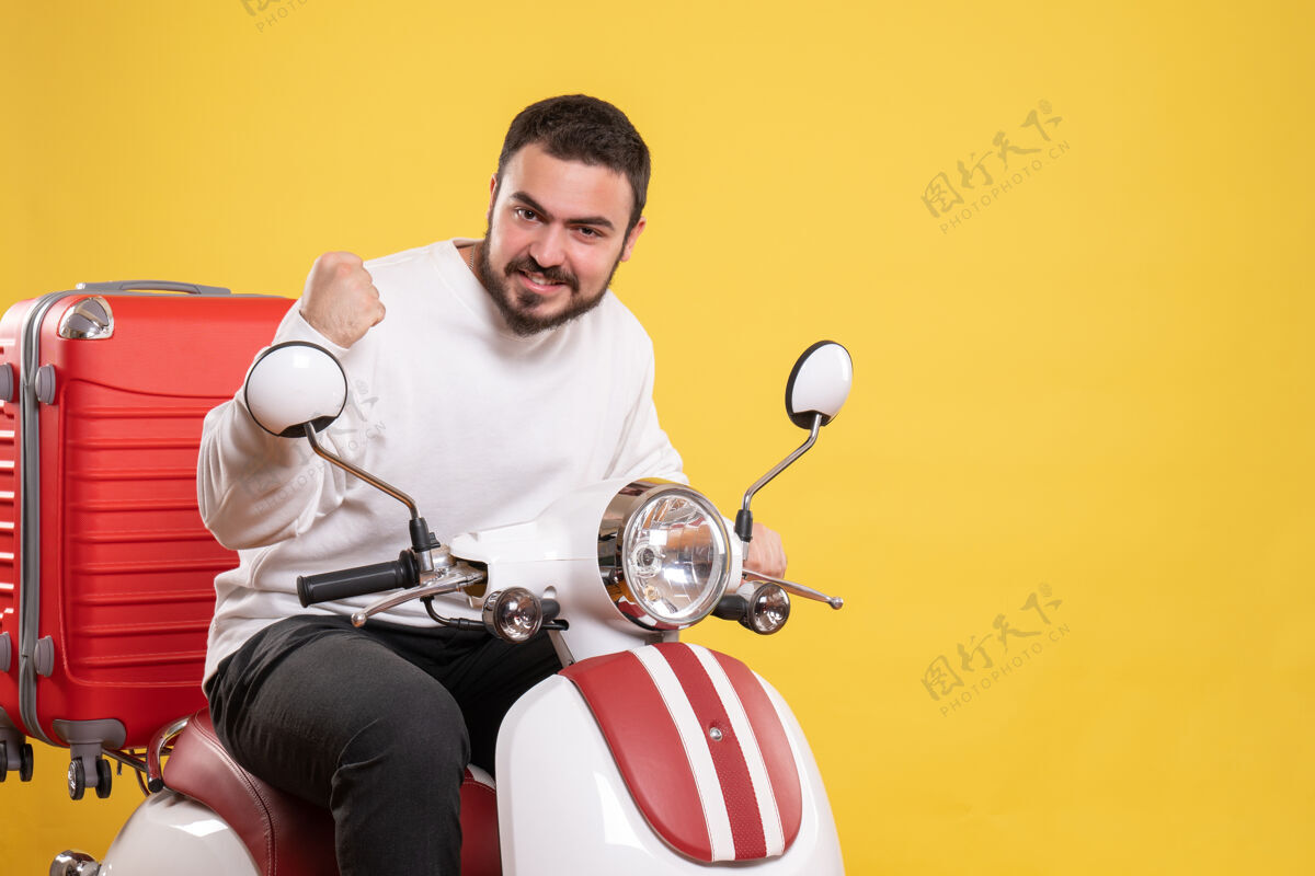 手提箱俯视图自豪的年轻人坐在摩托车上 手提箱上 享受他的成功孤立的黄色背景坐着微笑享受