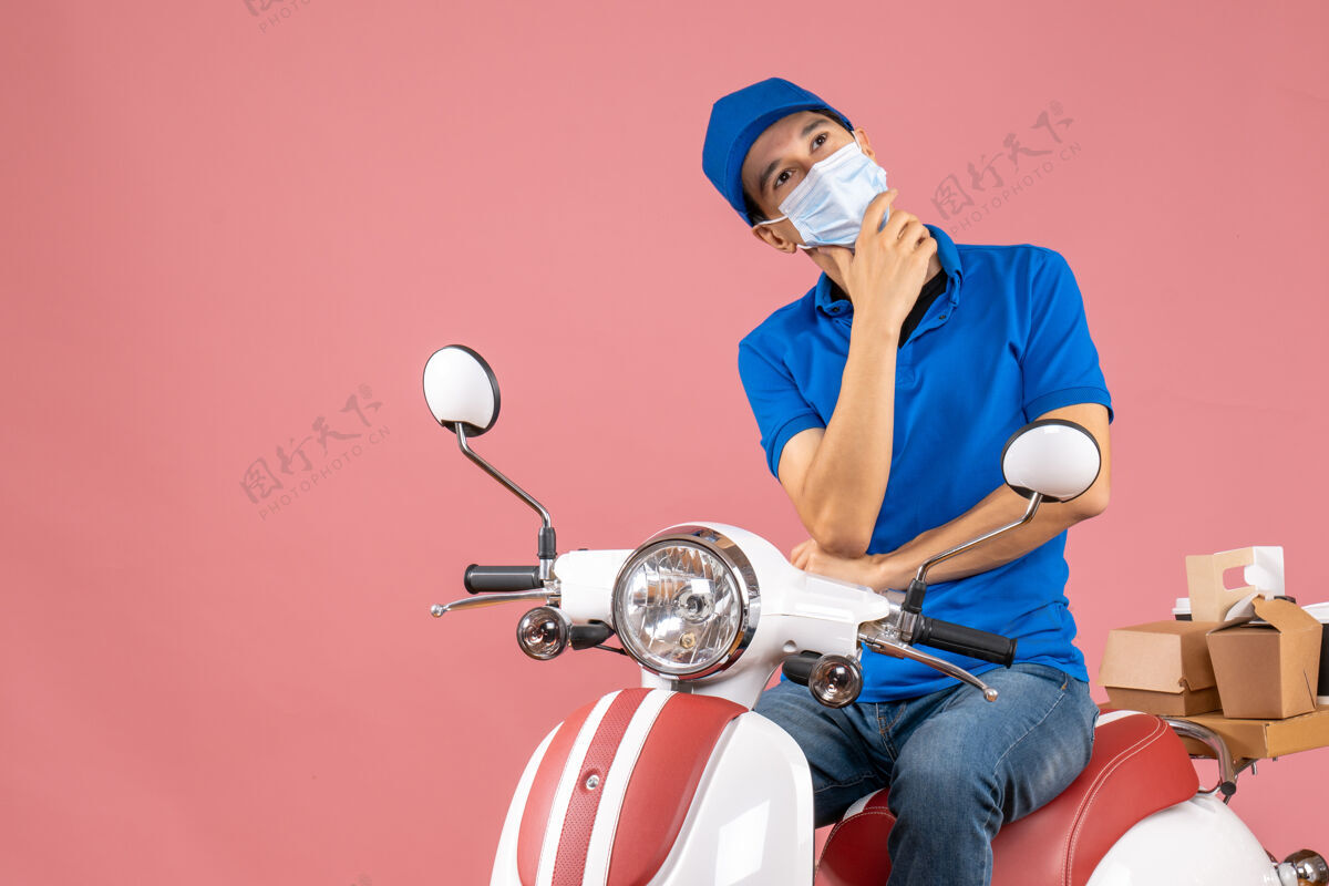 思想俯视图：戴着医用面罩戴着帽子的送货员坐在滑板车上 在柔和的桃色背景下沉思坐背景车辆