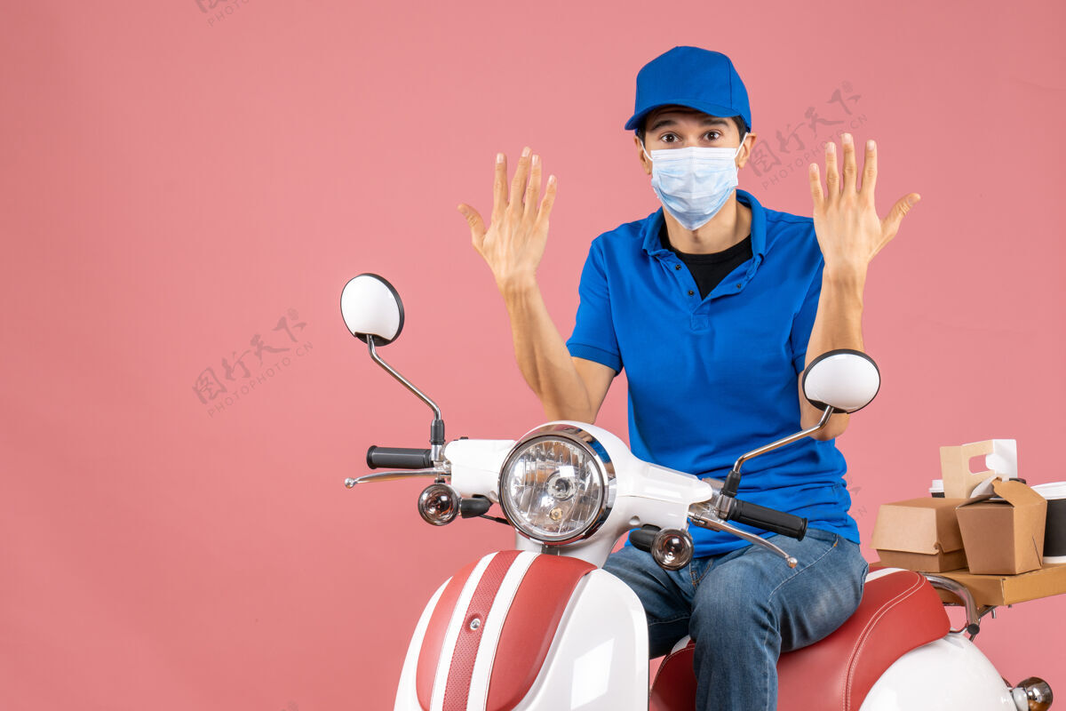 背景俯视图：戴着医用面罩戴着帽子的快递员坐在滑板车上 在柔和的桃色背景下感到好奇摩托车好奇面具