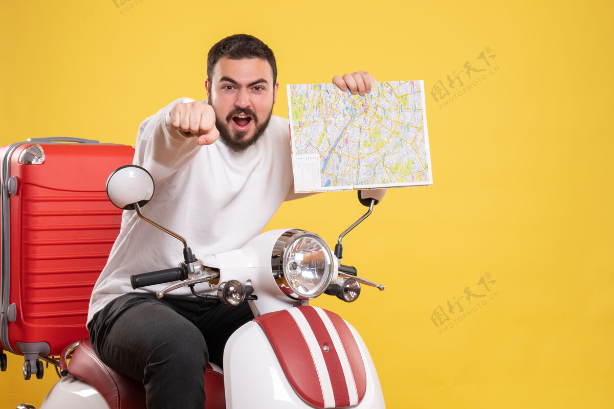成人顶视图野心勃勃的年轻人坐在摩托车上 手提箱上拿着地图 背景是孤立的黄色摩托车人物男性