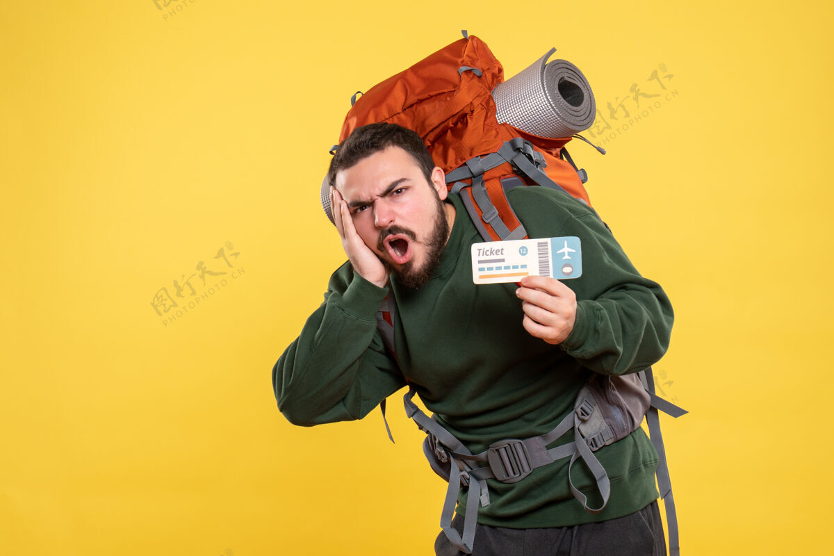 头发情绪紧张的旅行男子背着背包 拿着黄色背景上的票的正面视图人物交流背包