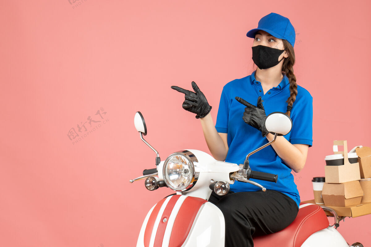 坐前视图困惑的快递女孩戴着医用面罩和手套坐在滑板车上传递粉彩桃背景的命令背景摩托车男