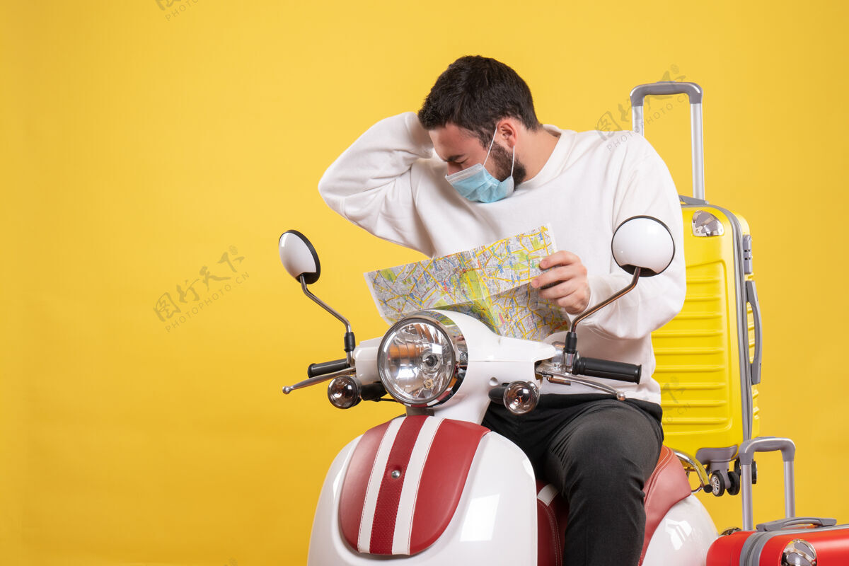 成人一个戴着医用口罩的年轻人坐在摩托车上 背着黄色手提箱 手里拿着地图 头痛不已旅行头痛摩托车