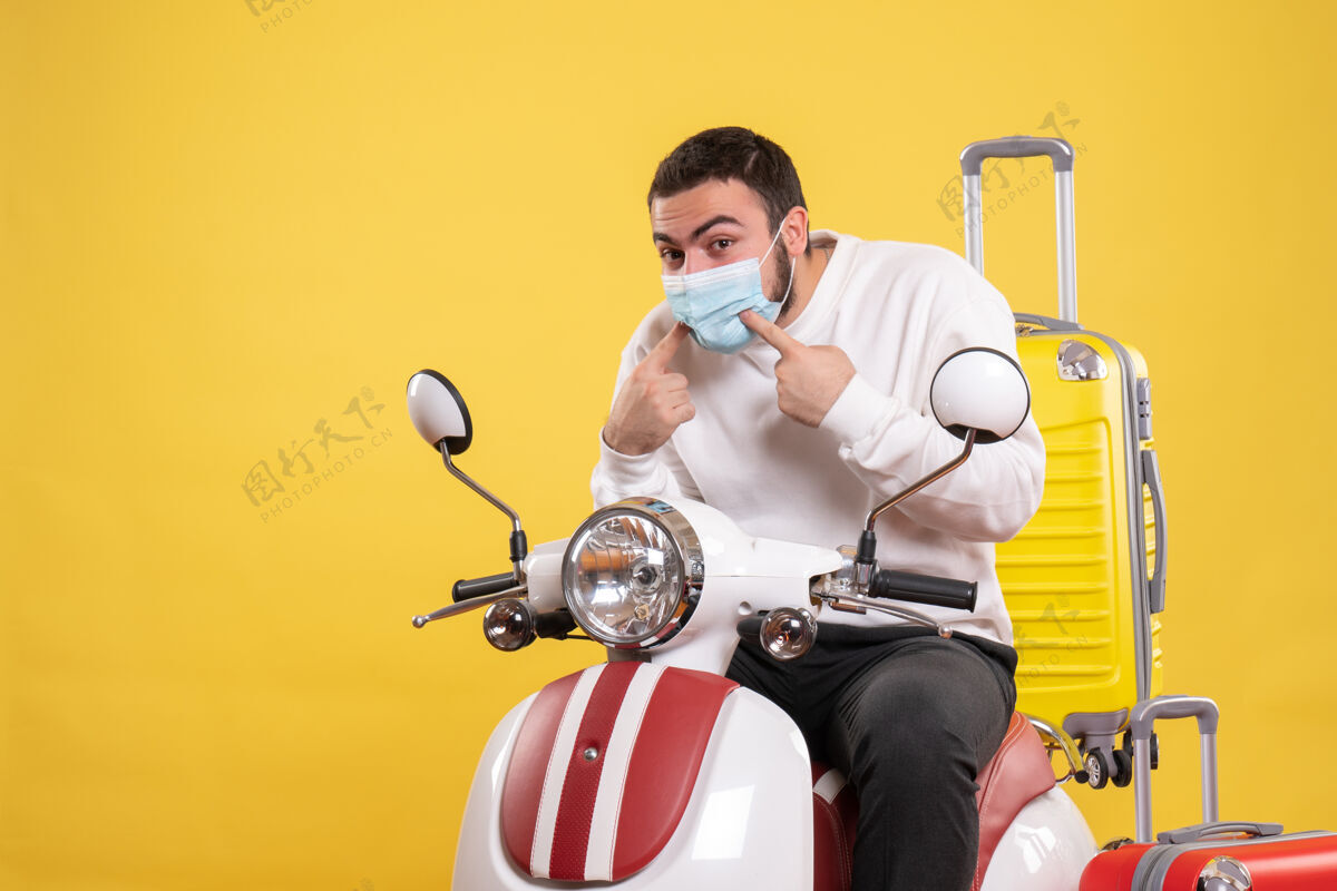 人旅行的概念与神奇的家伙在医疗面具坐在摩托车上与黄色手提箱在它的黄色手提箱人面具