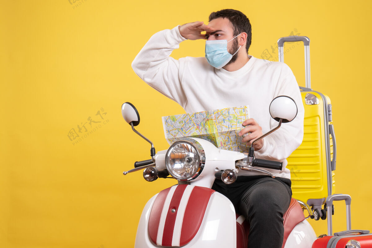 摩托车旅行概念 戴着医用面罩的年轻人坐在摩托车上 黄色手提箱在上面旅行人地图