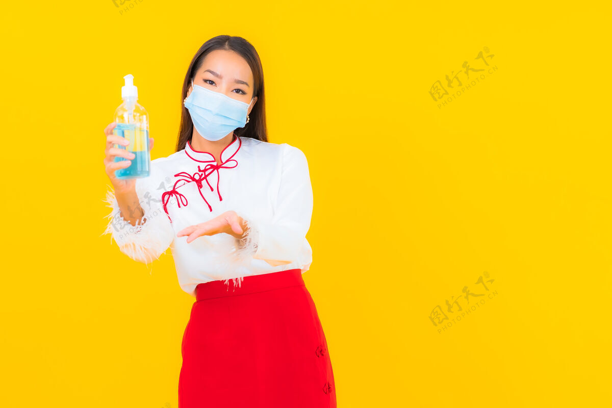 大流行肖像美丽的亚洲年轻女子戴上口罩 用酒精凝胶保护黄色的covid19流感办公桌成人