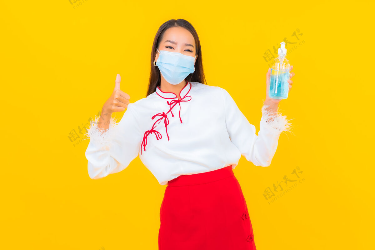 手肖像美丽的亚洲年轻女子戴上口罩 用酒精凝胶保护黄色的covid19中国流感呼吸道