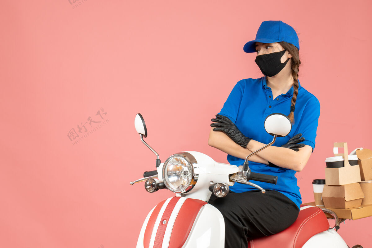 手套俯视图贴心的女快递员戴着医用口罩和手套坐在滑板车上传递粉彩桃的订单坐医疗桃