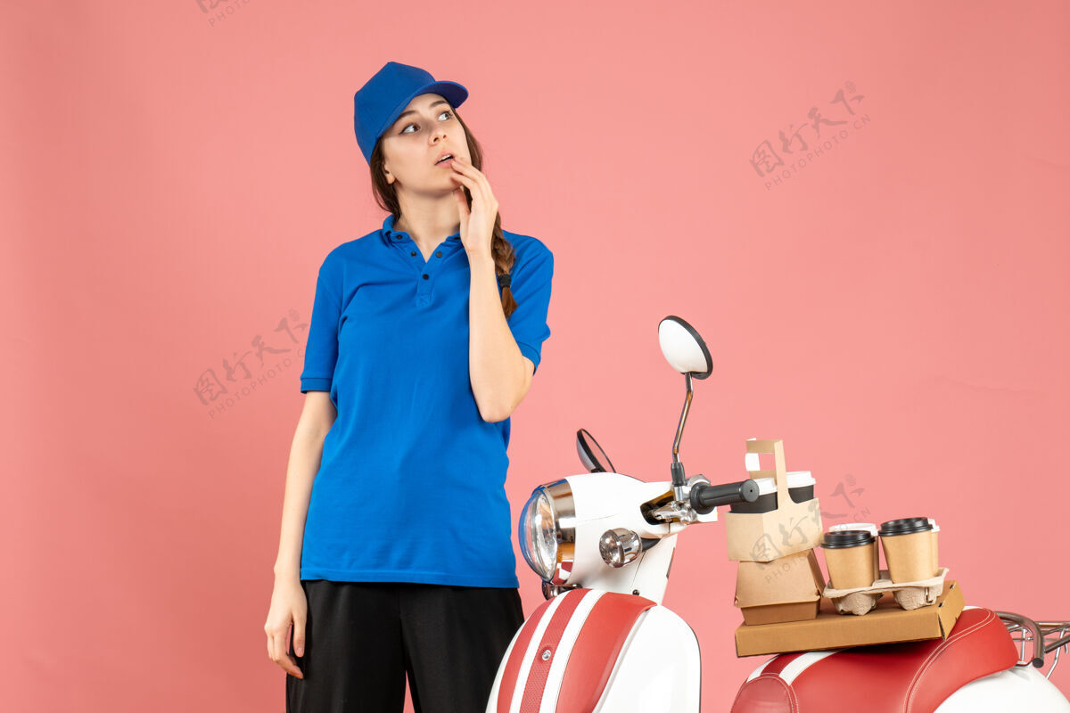 人俯视图：信使女士站在摩托车旁 车上有咖啡和小蛋糕 在柔和的桃色背景下沉思咖啡桃子工作