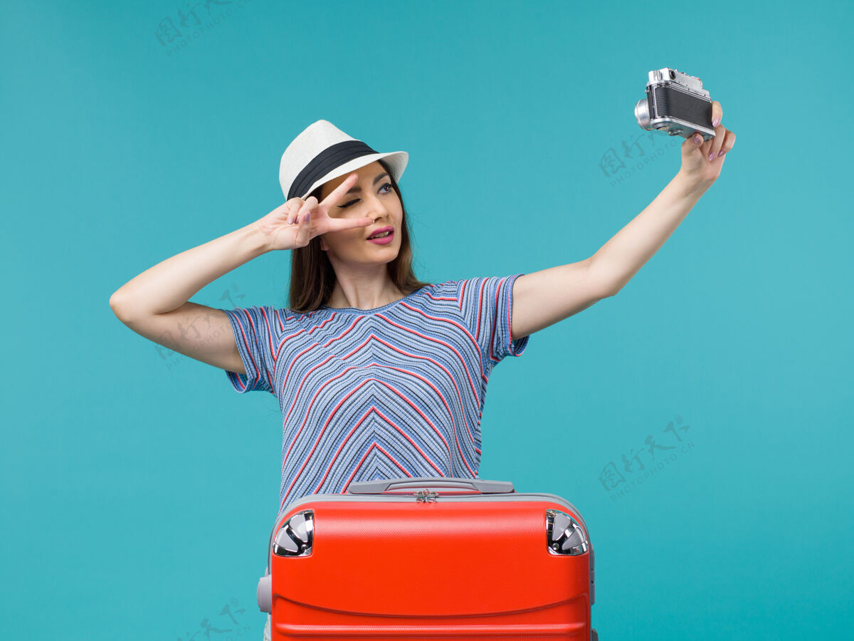 女人度假的女人拿着相机在蓝色上拍照相机手提箱航行