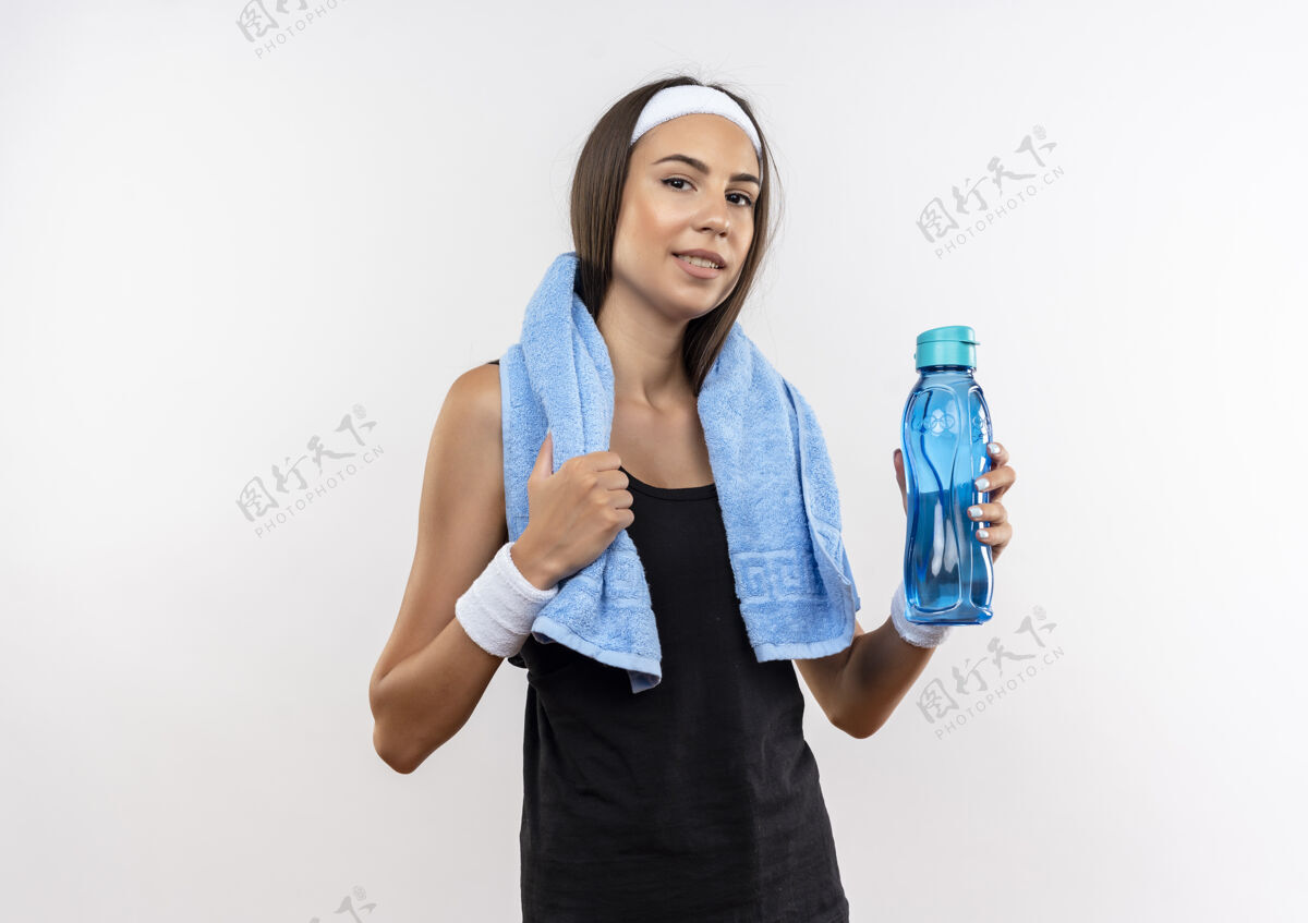 毛巾自信漂亮的运动女孩戴着头带和腕带拿着水瓶和毛巾围着她的脖子隔离在白色的墙上脖子女孩周围