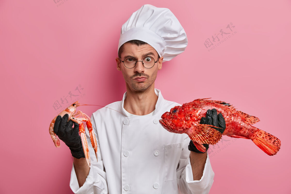 男性年轻帅气的厨师手拿生小龙虾帽子配料皱眉