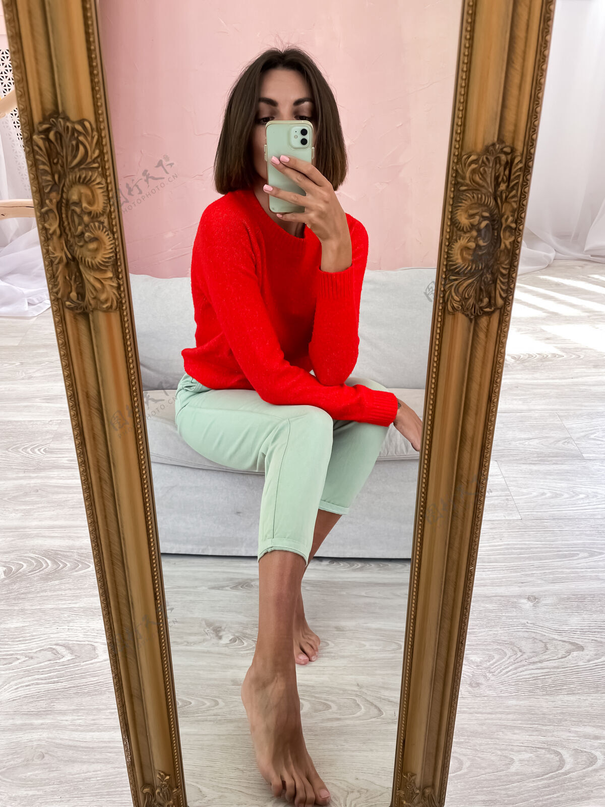 自拍穿着鲜红毛衣和薄荷绿裤子的时尚女性在家里对着手机对着镜子自拍手机运动挥舞