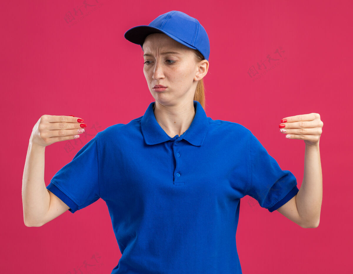 年轻穿着蓝色制服 戴着帽子的年轻送货员 看上去自信满满 双手像是站在粉色墙壁上拿着什么东西立场信心女孩