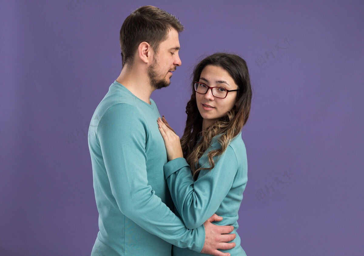 拥抱年轻漂亮的情侣穿着蓝色休闲服快乐开朗的男人和女人拥抱幸福的爱情庆祝情人节站在紫色的墙上欢呼年轻休闲