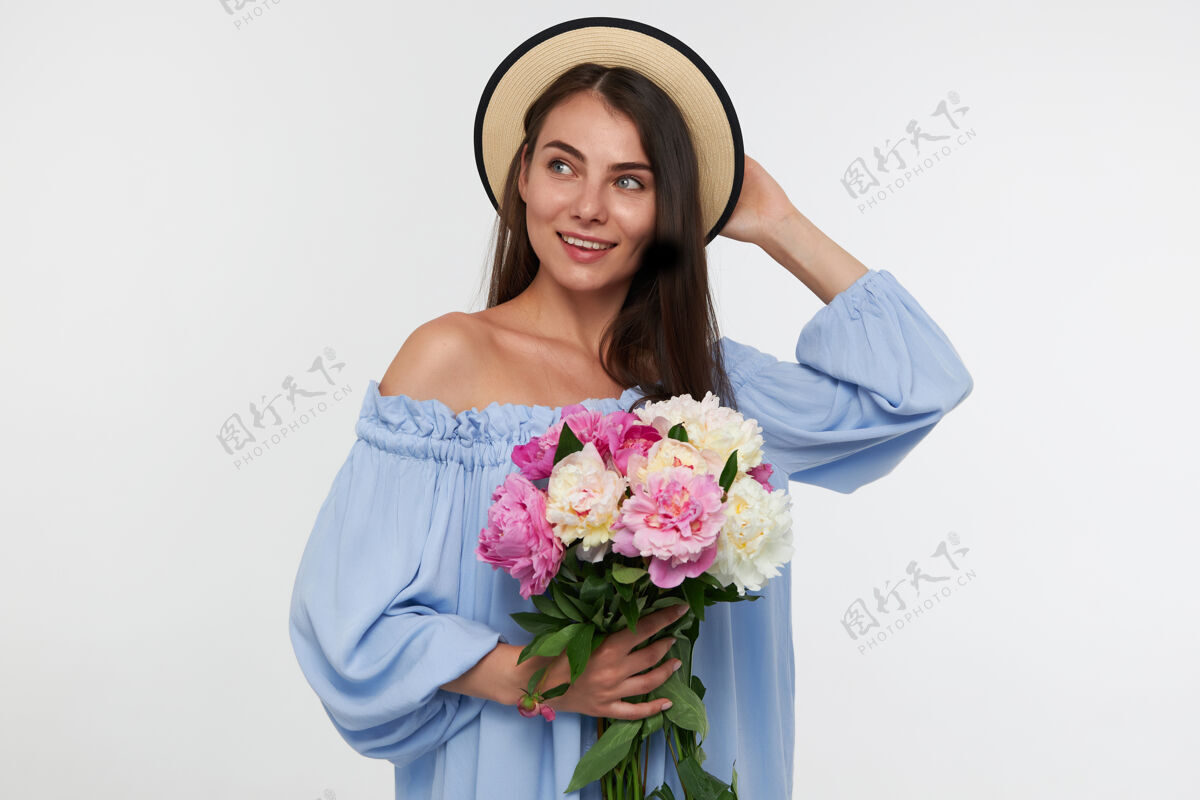 成人有魅力的女孩的肖像 长黑发戴着帽子和蓝色漂亮的裙子拿着一束花和触摸一顶帽子花束完美美丽