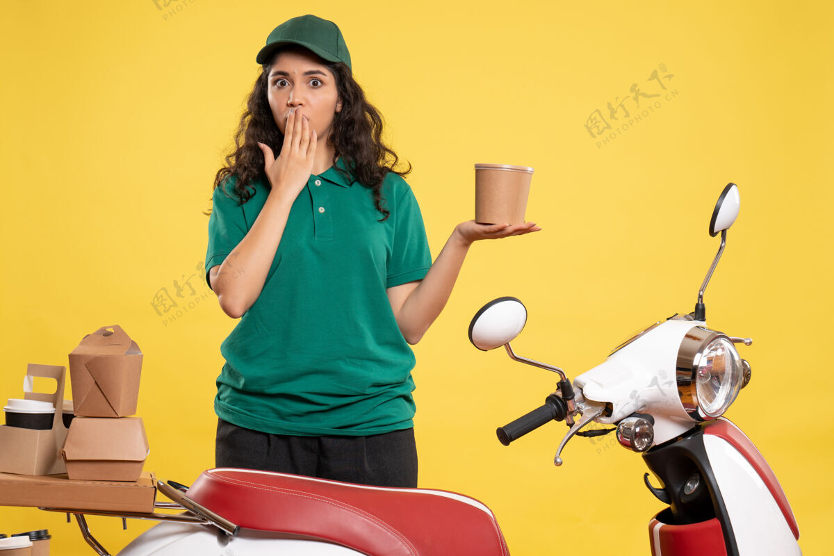 人正面图身着绿色制服的女快递员 黄色背景上有甜点 工作颜色 工作递送女工食品工作设备女信使