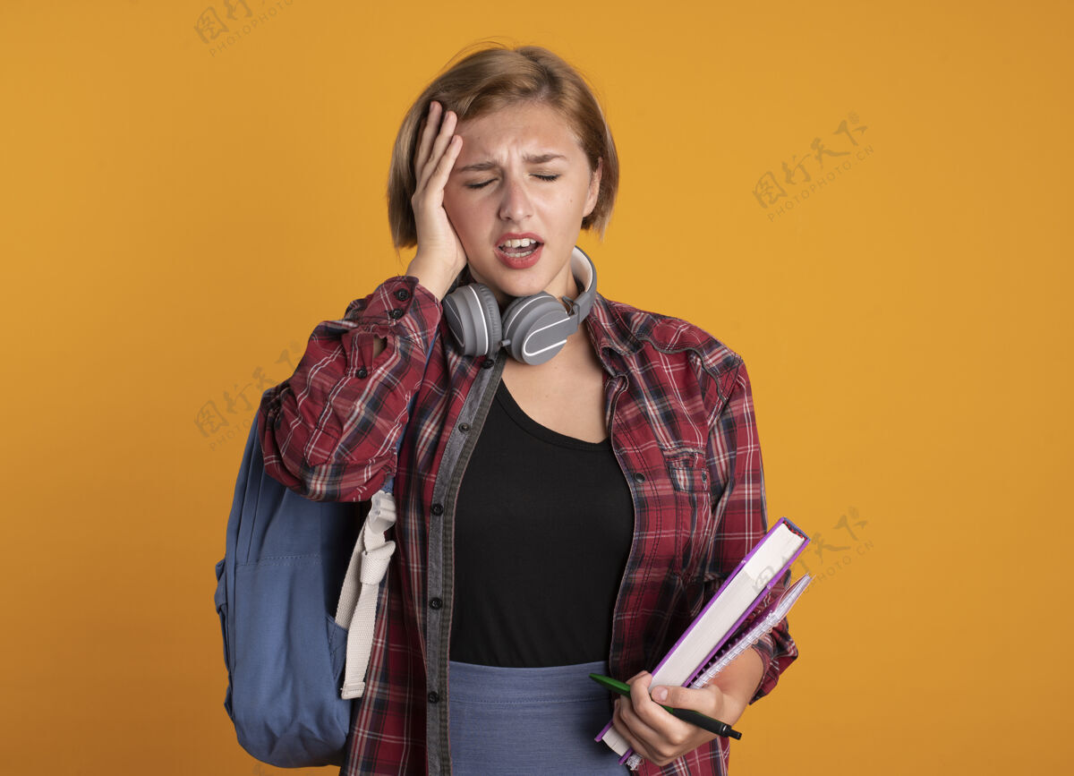 穿带着耳机 背着背包 手放在头上 手里拿着书和笔记本的年轻斯拉夫女学生背包空间年轻
