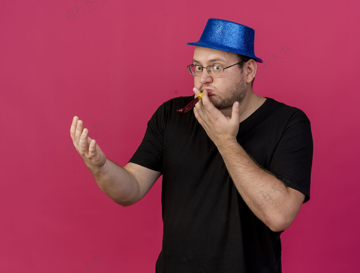 打开惊讶的成年斯拉夫人戴着眼镜 戴着蓝色派对帽 手张开 吹着派对哨子粉色成人光学