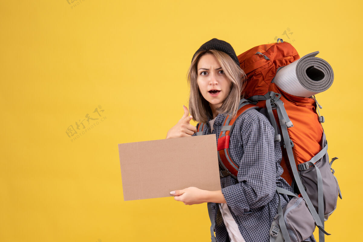 女旅客背着背包拿着硬纸板指着摄像机的女旅行者纸板人女士