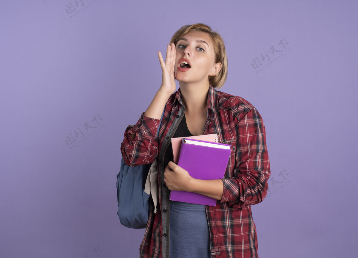 女孩震惊的年轻斯拉夫学生女孩背着书包 手放在嘴边 手里拿着书和笔记本背包嘴持有