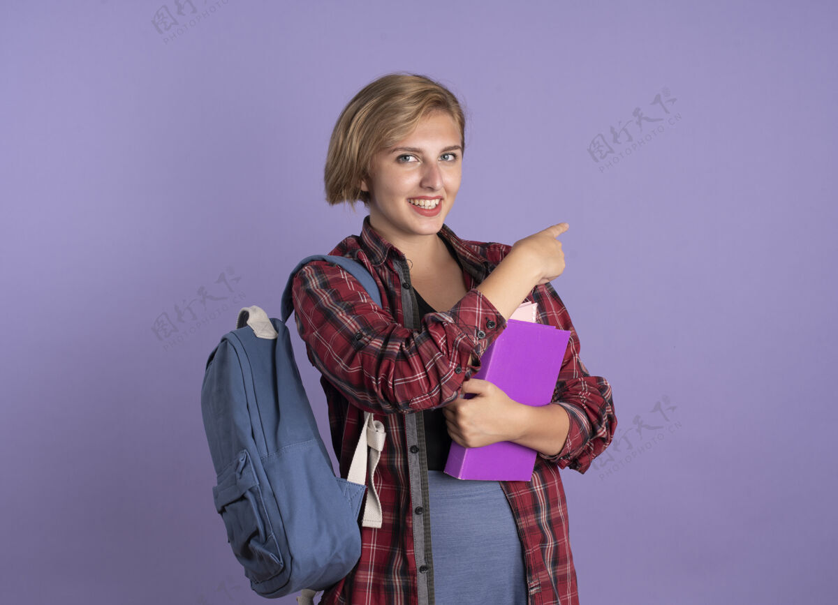 穿微笑着的年轻斯拉夫女学生背着书包拿着书和笔记本指着身边背包空间紫色