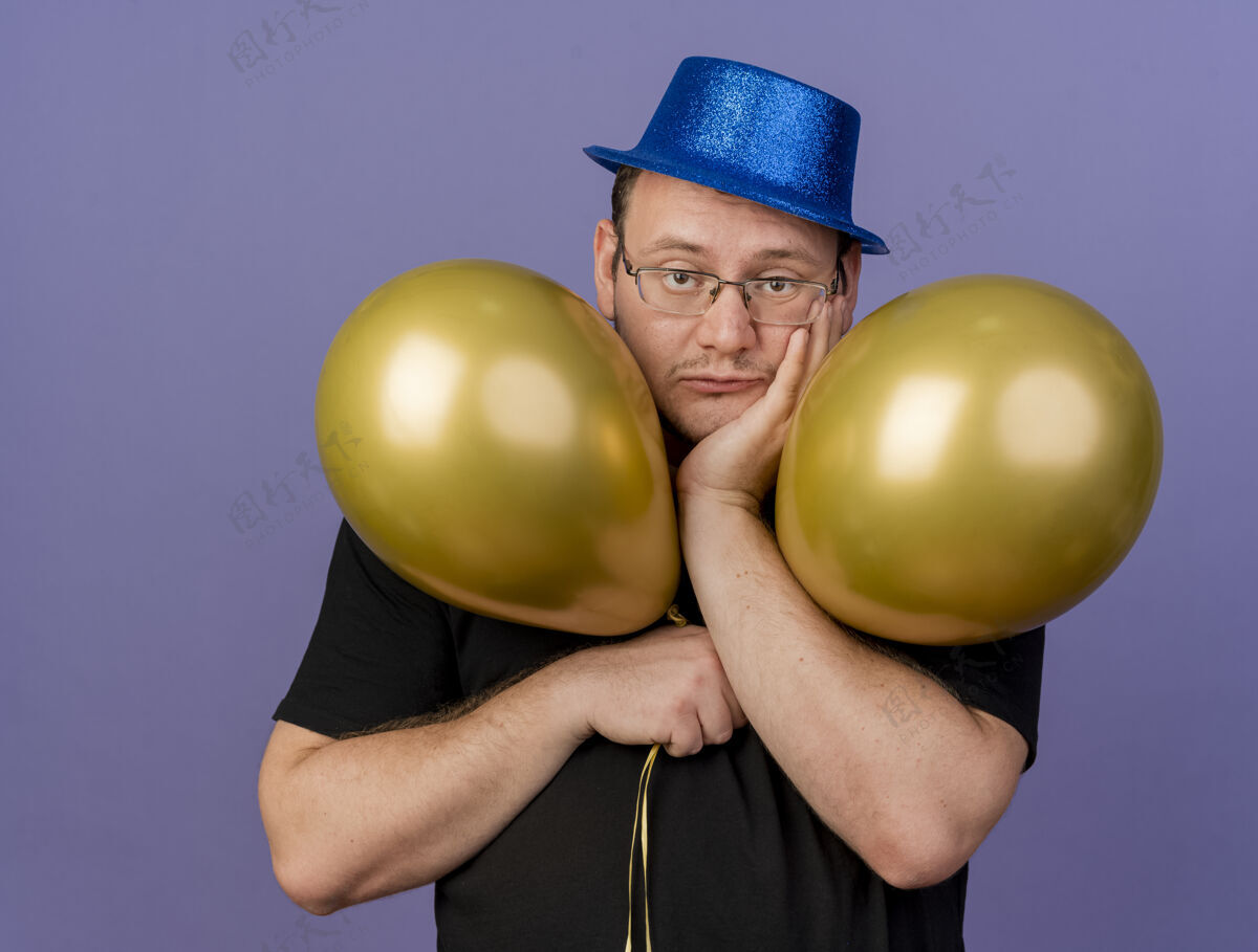斯拉夫失望的成年斯拉夫人戴着眼镜 戴着蓝色派对帽 手放在下巴上 手里拿着氦气球穿手聚会