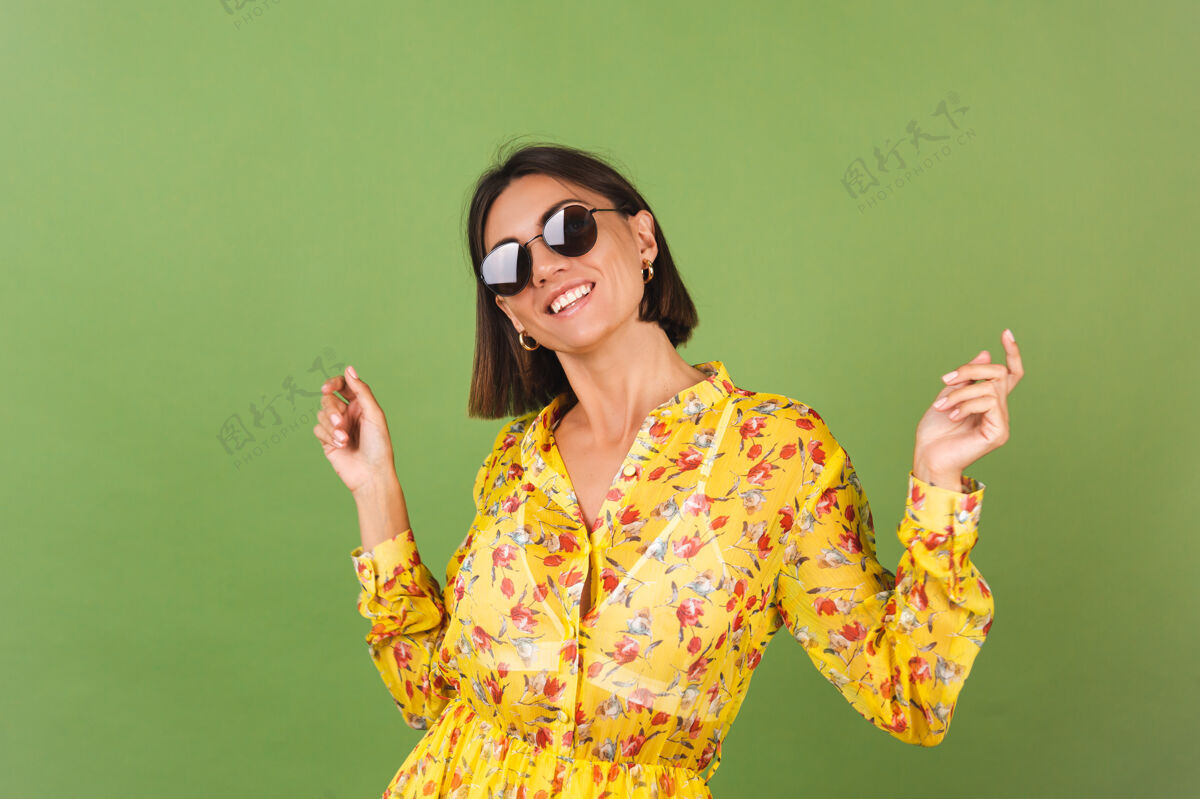明亮穿着黄色夏装 戴着墨镜的漂亮女人 绿色的工作室 快乐积极快乐的情绪服装肖像舞蹈