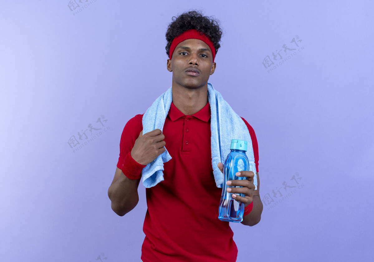 瓶子自信的年轻美国黑人运动男子戴着头带和腕带拿着水瓶和毛巾在肩上穿男人腕带