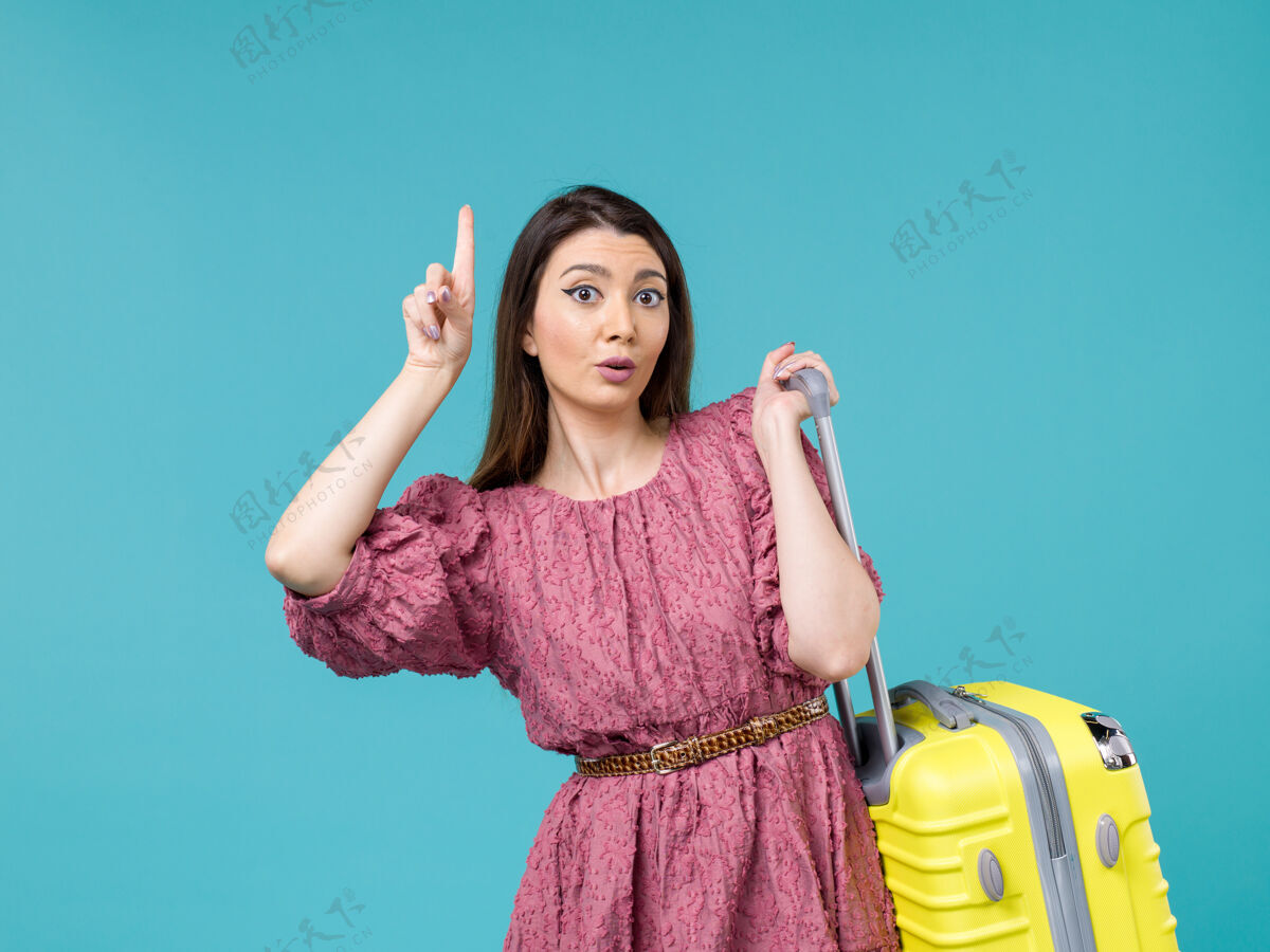 漂亮正面图年轻女子带着她的黄色袋子在蓝色背景上度假夏天的女人旅行人类旅行海洋人年轻的女人人
