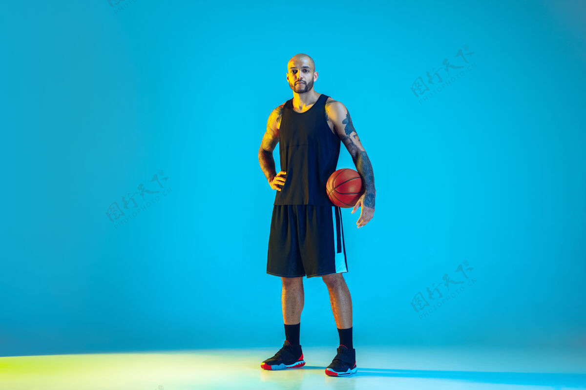 冠军年轻的篮球队员穿着运动服训练 在运动中练习 在霓虹灯下的蓝色墙壁上运动健康球场球