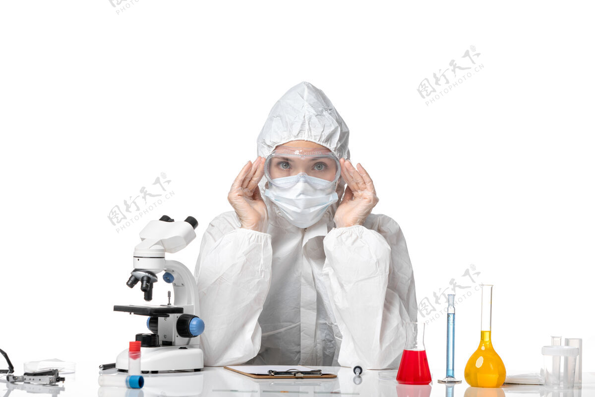 药正面图年轻女医生穿着防护服带着口罩坐在白色办公桌上传播病毒套装成人面罩