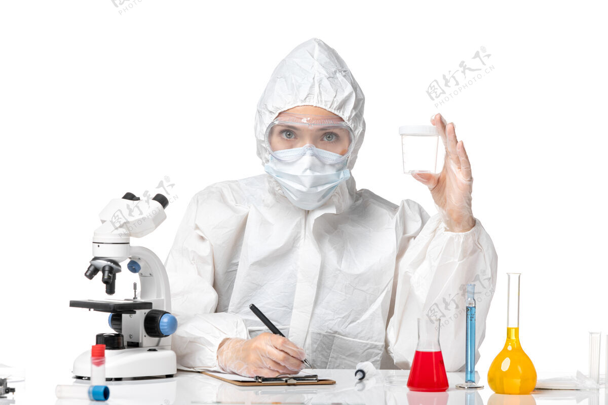 大流行正面图年轻的女医生穿着防护服 戴着口罩 因为拿着一个瓶子 在白色的背景上写着流行的病毒套装防护药品