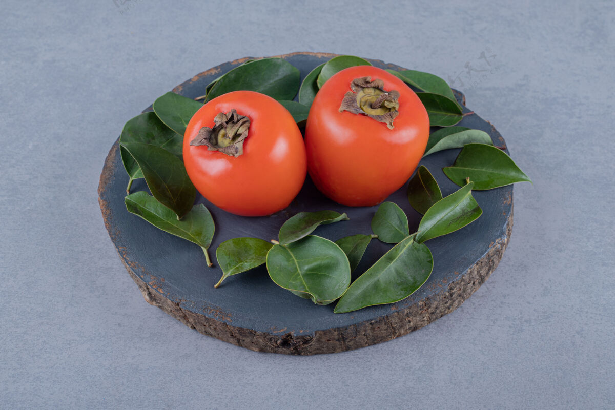 异国情调两个新鲜的柿子 叶子放在灰色的木板上健康柿子切