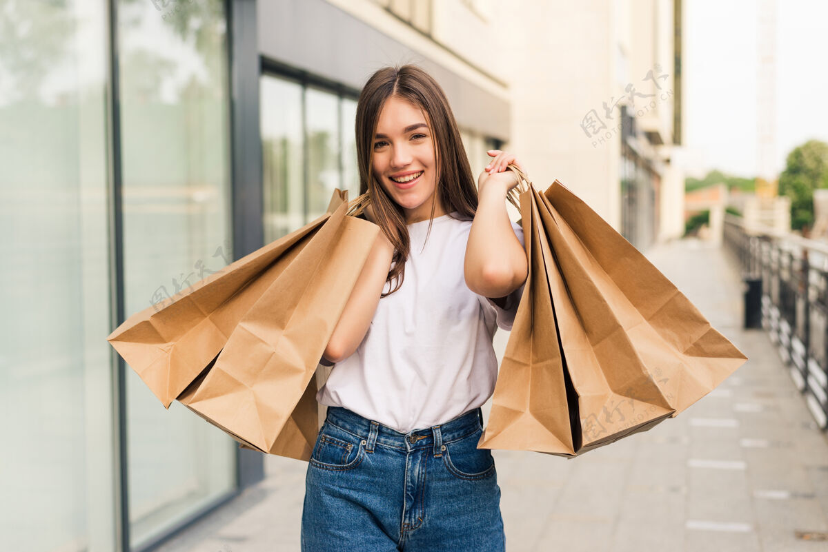 夏天美丽的年轻女子拿着购物袋 在户外微笑着消费主义购物享受