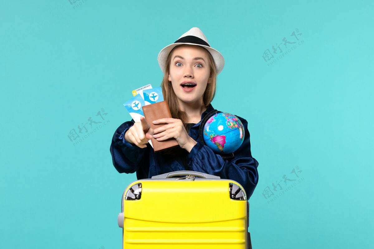 肖像前视图年轻女子拿着机票和地球仪在淡蓝色背景的飞机上航行海上度假之旅旅程票微笑
