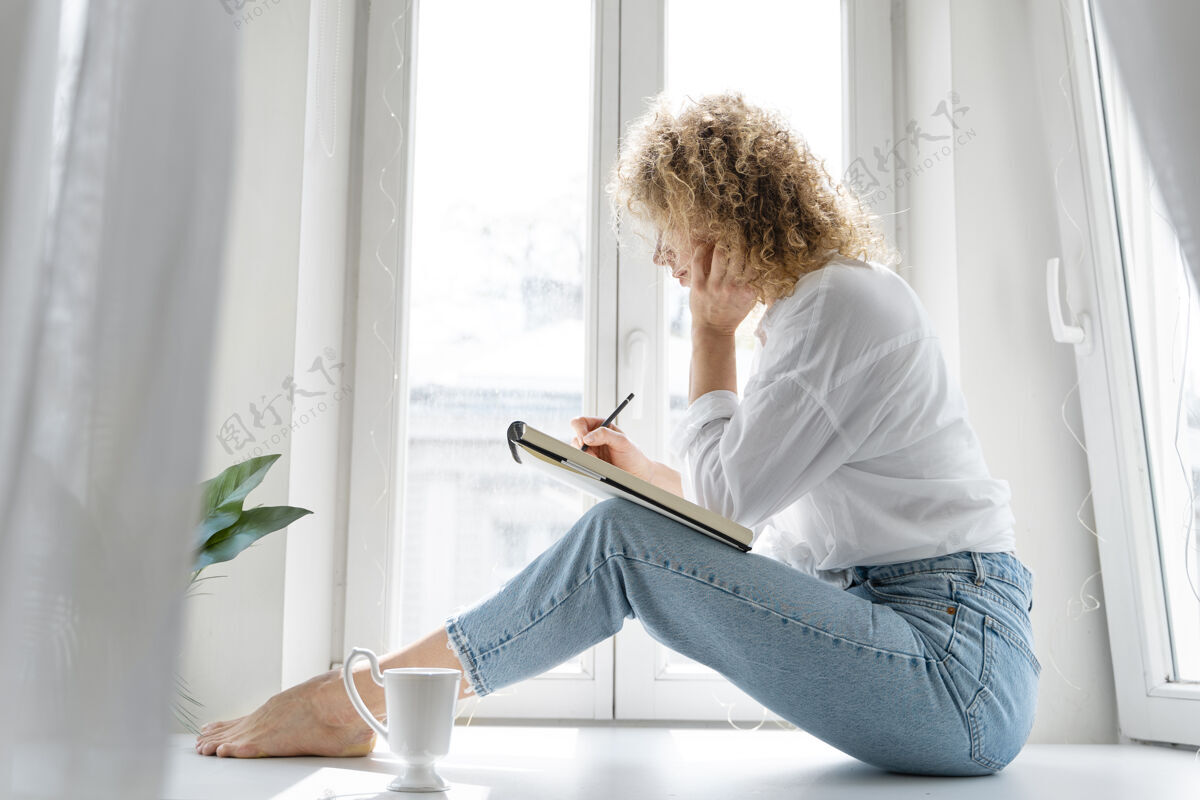 休闲一位年轻女子在家里靠窗画画的侧视图家庭艺术家房子