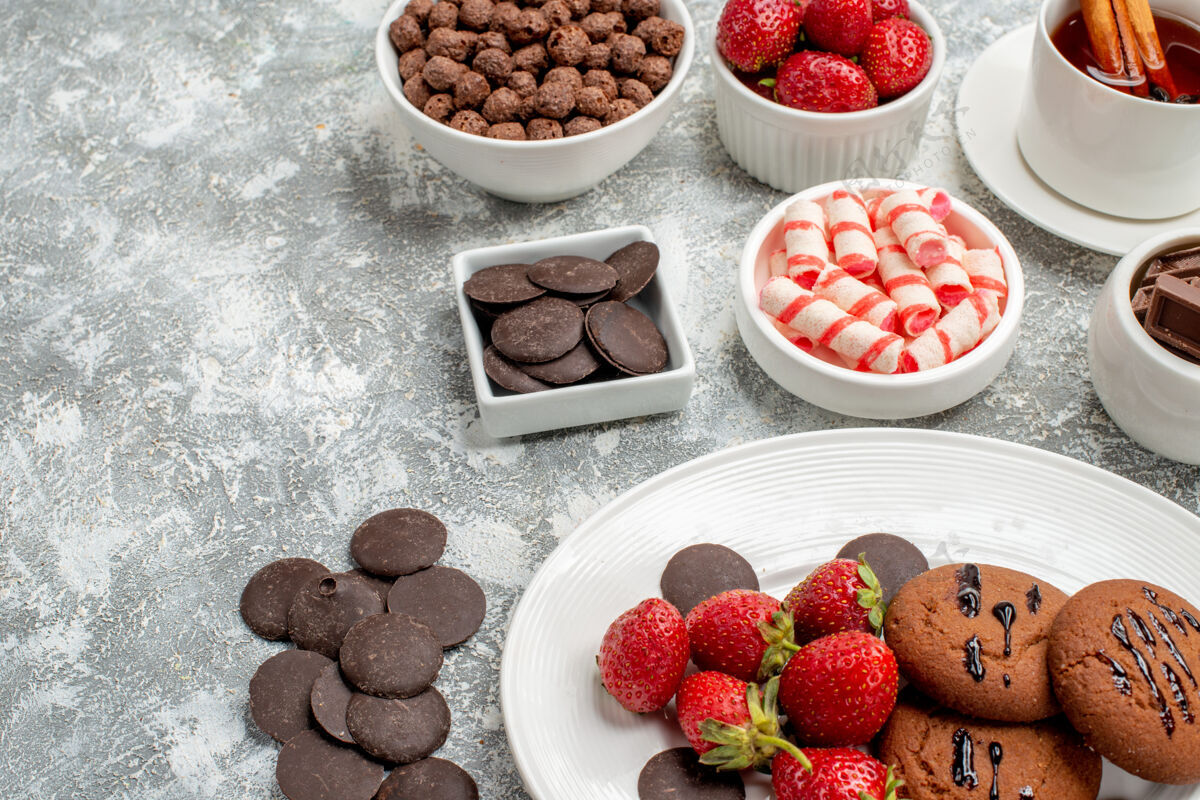 浆果底部特写饼干草莓和圆形巧克力放在椭圆形的盘子里 糖果草莓巧克力麦片和肉桂茶放在灰白色的桌子上椭圆形盘子草莓