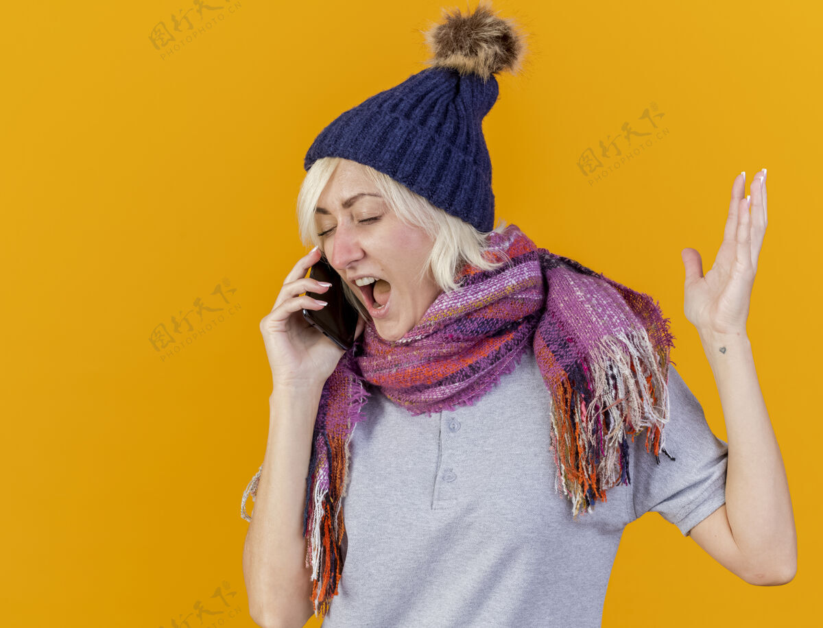 年轻恼怒的年轻金发病斯拉夫妇女戴冬季帽子和围巾站电话金发举起