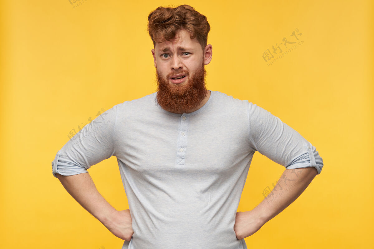 装束一个留着红胡子的年轻人的画像 双手放在臀部 对黄色的脸上恼怒的表情感到困惑和不快表情困惑不快乐