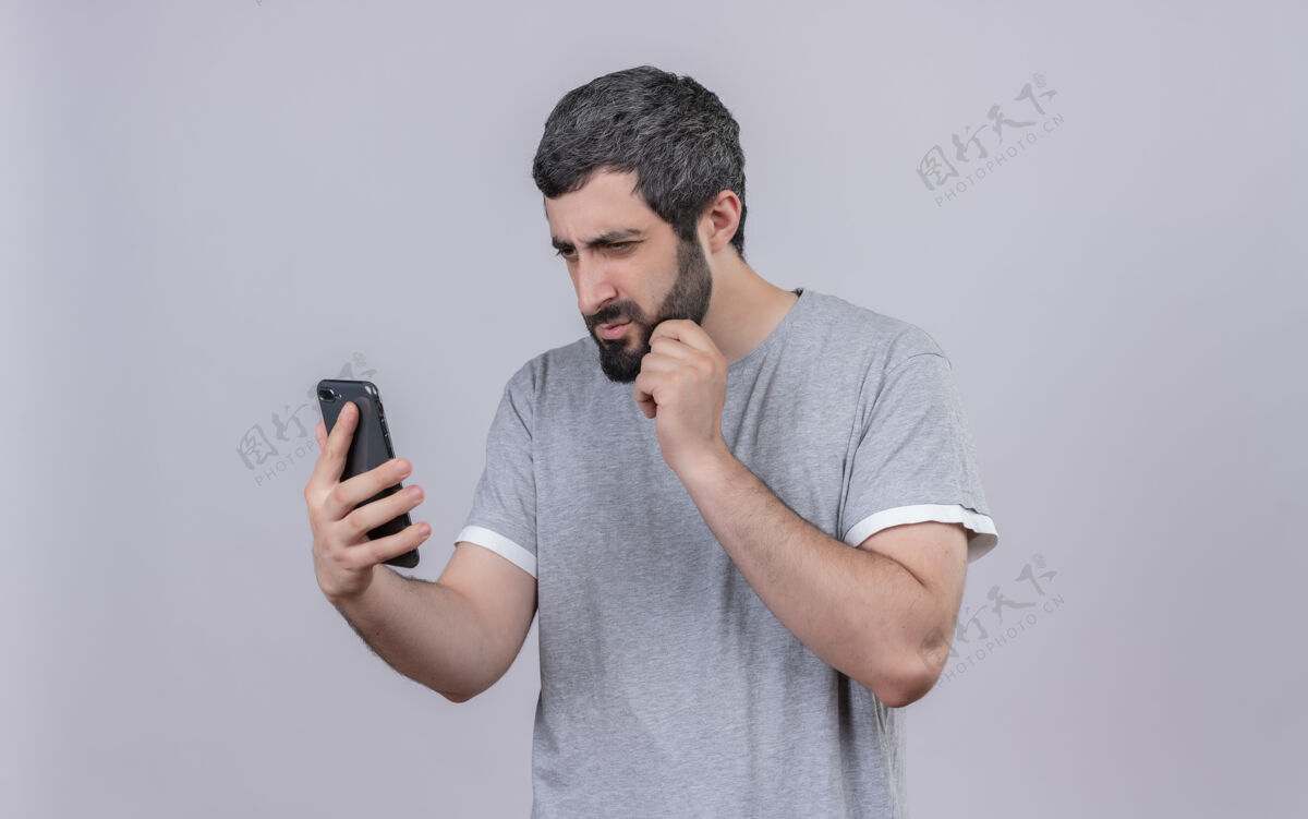 脸体贴的年轻帅哥抱着手机 看着手机 抚摸着隔离在白墙上的下巴电话手机帅